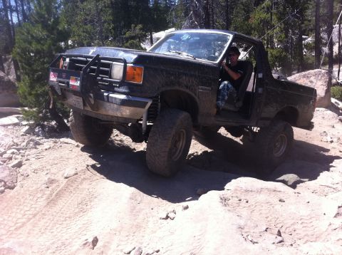 1990 Ford Bronco - A black Ford Bronco navigates a challenging rocky trail with its doors open.