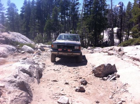 1990 Ford Bronco - Ford Bronco tackling a challenging rocky trail in a wooded area.