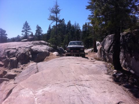1990 Ford Bronco - An SUV navigates a , rocky path through a forested area under a clear blue sky.
