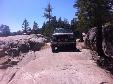 1990 Ford Bronco - A black Ford Bronco navigates a rocky trail under a clear blue sky.