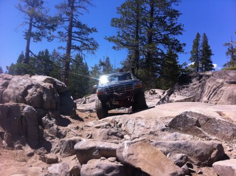 1990 Ford Bronco - A dark blue Ford Bronco tackles a challenging rocky terrain on an off-road trail.