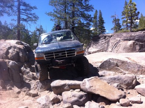 1990 Ford Bronco - A dark blue 1992 Ford Bronco tackles a challenging rocky trail, demonstrating its off-road capabilities.
