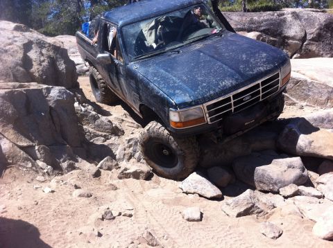 1990 Ford Bronco - Ford Bronco tackling a challenging off-road course with large rocks and uneven terrain.