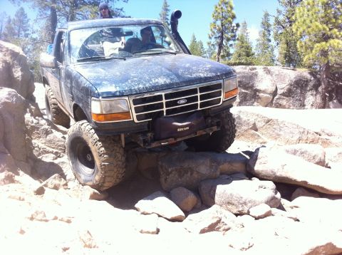 1990 Ford Bronco - This truck is on a trail with large rocks and trees. The front of the vehicle is visible.
