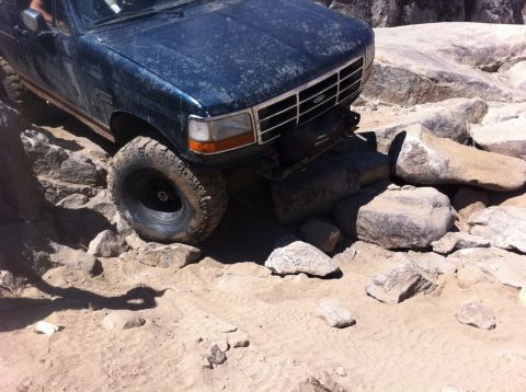 1990 Ford Bronco - A dark blue Ford truck is shown off-roading over large rocks.