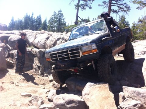 1990 Ford Bronco - This modified SUV, likely a 1992 Ford Bronco, tackles a challenging rocky trail with a snorkel installed for off-road capability.