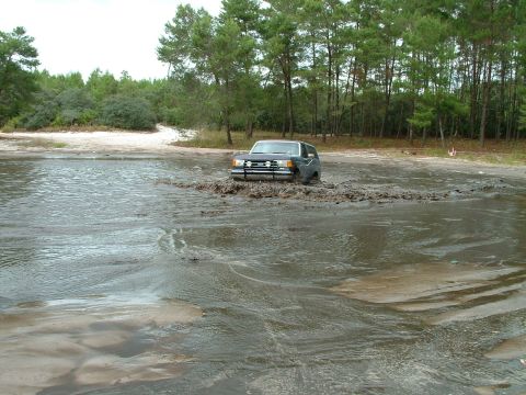 1995 Ford Bronco - A dark SUV navigates through a muddy water obstacle.