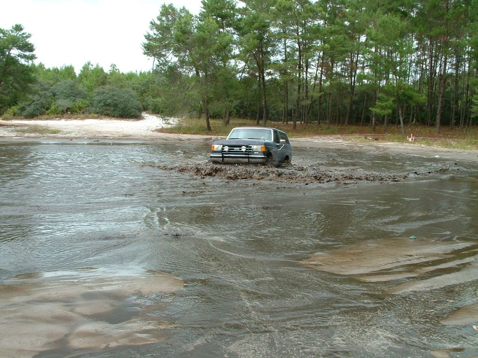 Dark SUV driving through mud and water, front view
