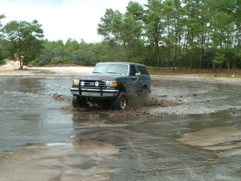 1995 Ford Bronco - This dark blue SUV navigates through a muddy puddle, showing off its off-road capabilities.