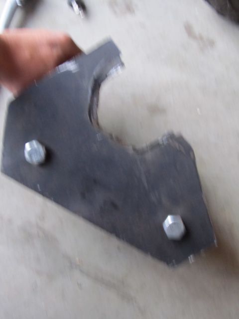 1984 Ford Bronco - A metal bracket with two hex bolts is held by a hand against a concrete surface.