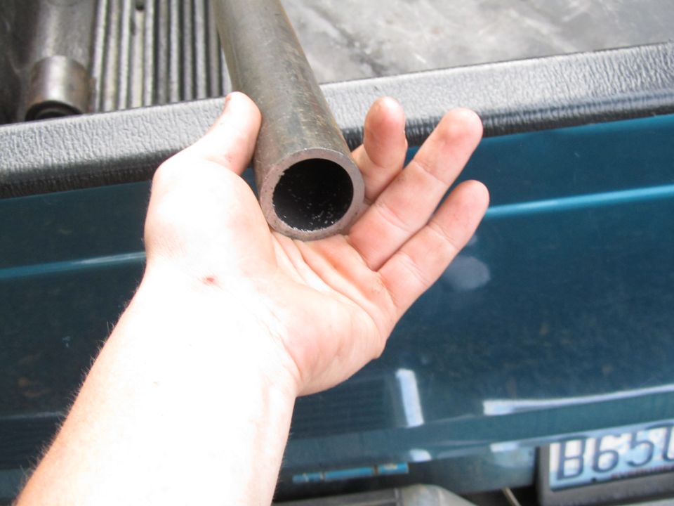 Hand holding a section of metal pipe over the bed of a teal pickup truck