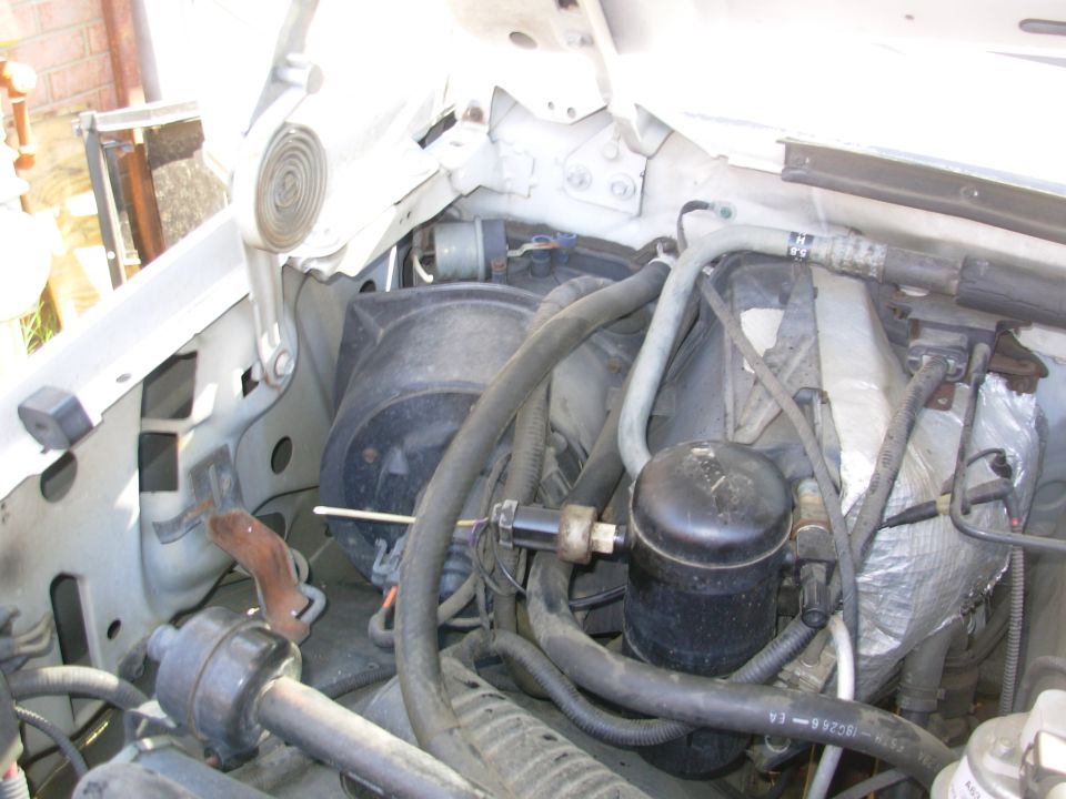 Engine bay of a white vehicle showing A/C components and wiring