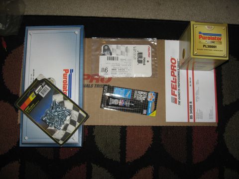 1994 Ford Bronco - Freshly bought engine service parts laid out on a patterned rug: a Fel-Pro OS 34508 R oil pan gasket set, Fel-Pro 72516 gasket in a blister…