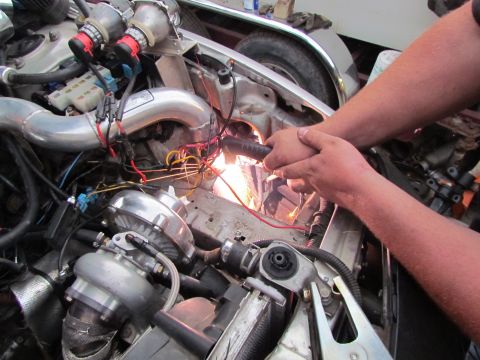1995 Ford Probe - Mechanics are working on the engine bay, which features a twin-turbo setup and custom exhaust piping.