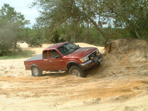 1995 Ford Bronco - Red Toyota Tacoma pickup truck navigating sandy terrain off-road.
