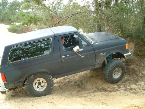 1995 Ford Bronco - A Ford Bronco navigates a sandy incline, its off-road capabilities with raised suspension and large tires.