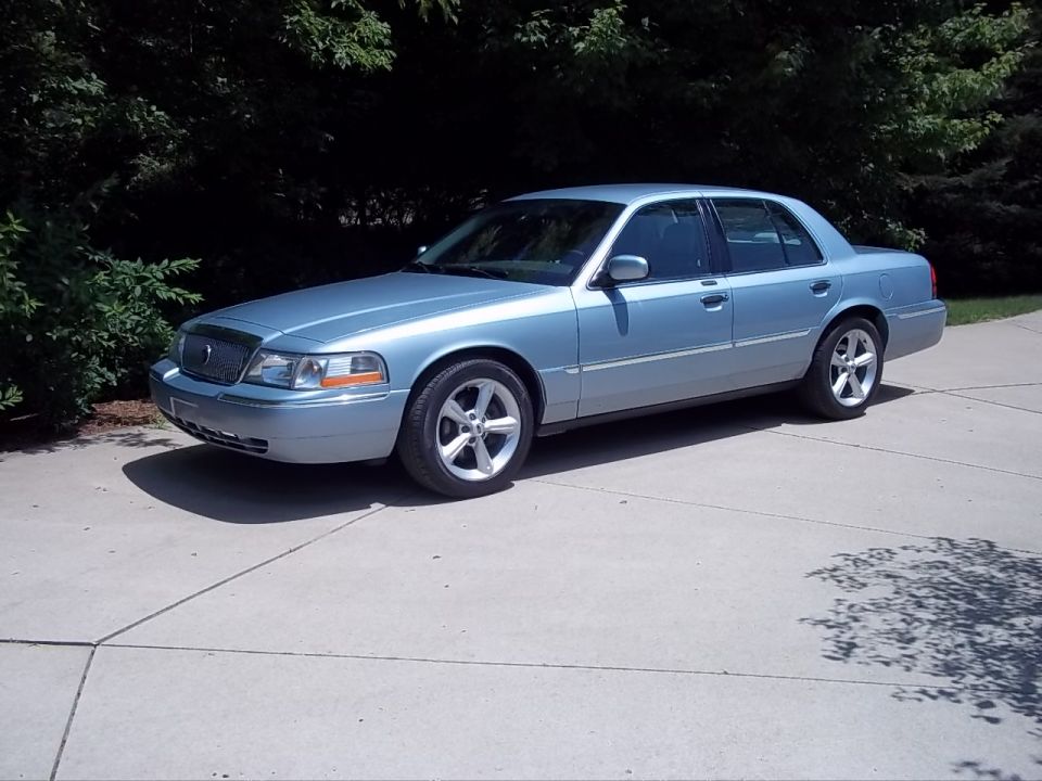 Light blue 2003 Mercury Grand Marquis sedan parked on a concrete driveway, side view