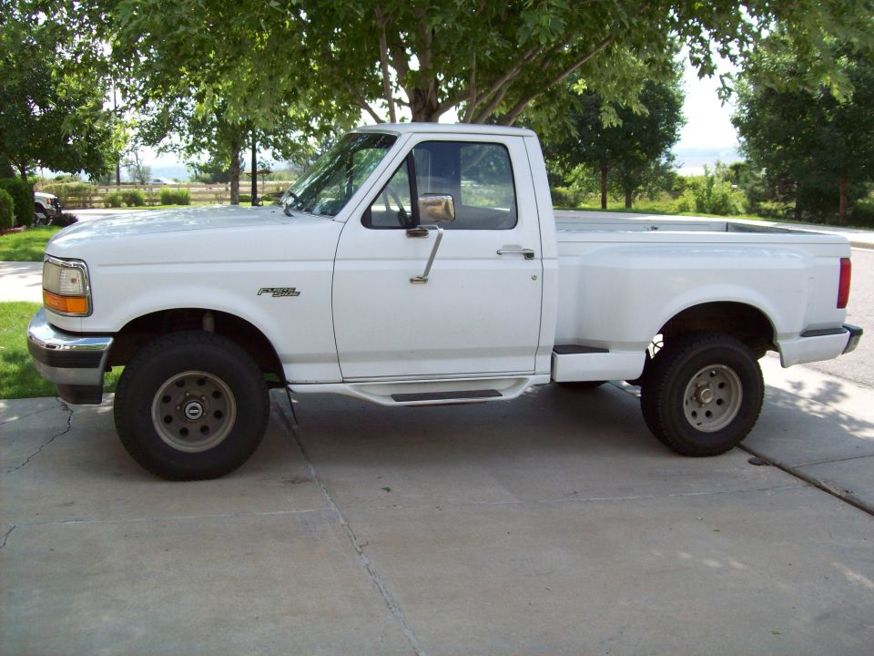 White single-cab Ford F-150 stepside pickup parked in side profile on a driveway