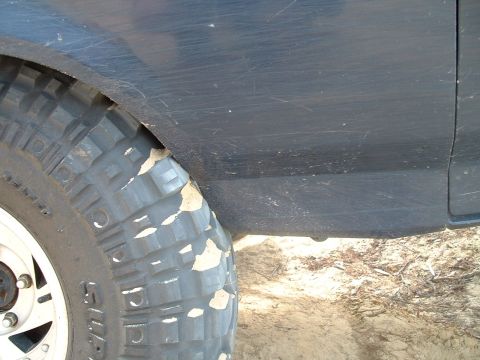 1995 Ford Bronco - Close-up of a dark blue SUV's fender and tire, showing off-road use.