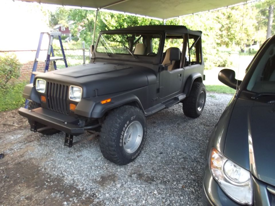 Black 1993 Jeep YJ parked under a carport next to another vehicle