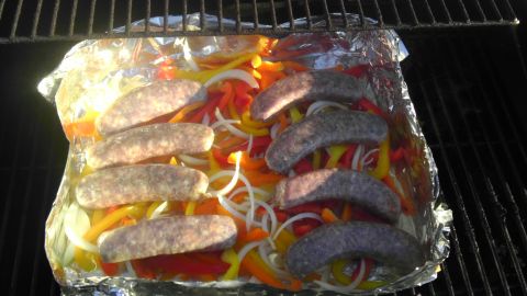 1989 Ford Bronco - Sausages and sliced bell peppers and onions are arranged in foil on a grill grate.