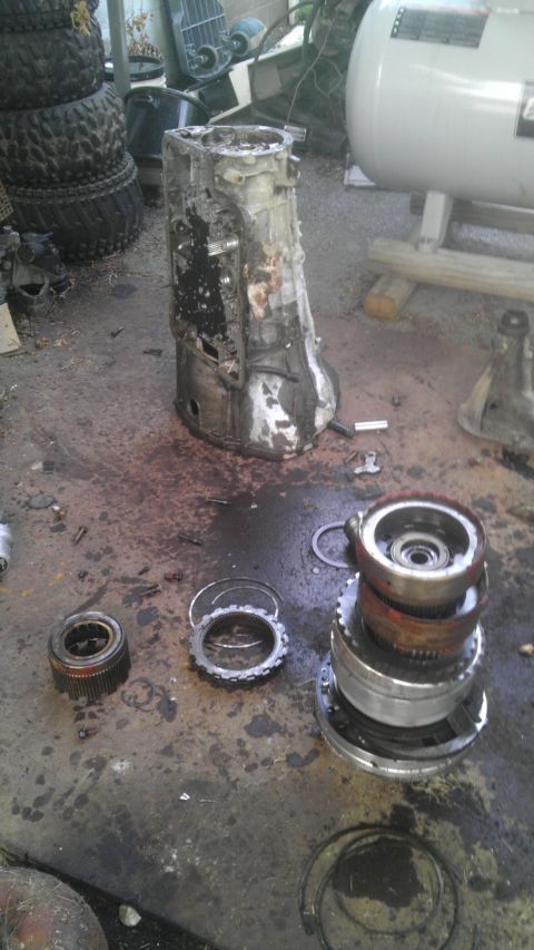 1989 Ford Bronco - A heavily damaged transmission case and its internal parts are laid out on a workshop floor.