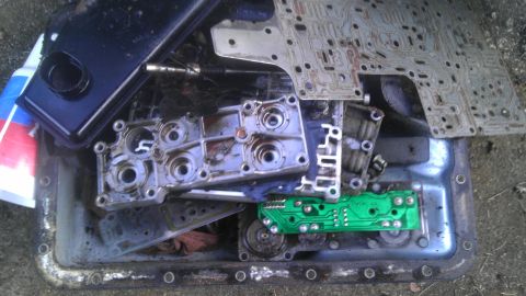 1989 Ford Bronco - Disassembled transmission parts, including a valve body, filter, and circuit board, are laid out in a pan.