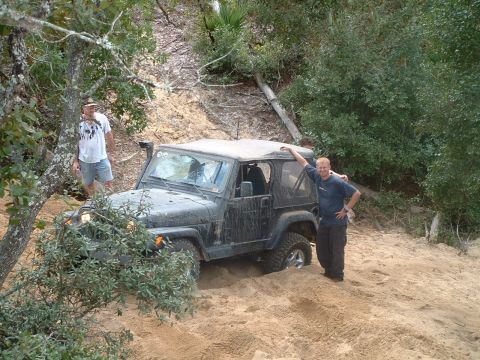 1995 Ford Bronco - Two men stand by a Jeep Wrangler that is stuck in a sandy off-road area.