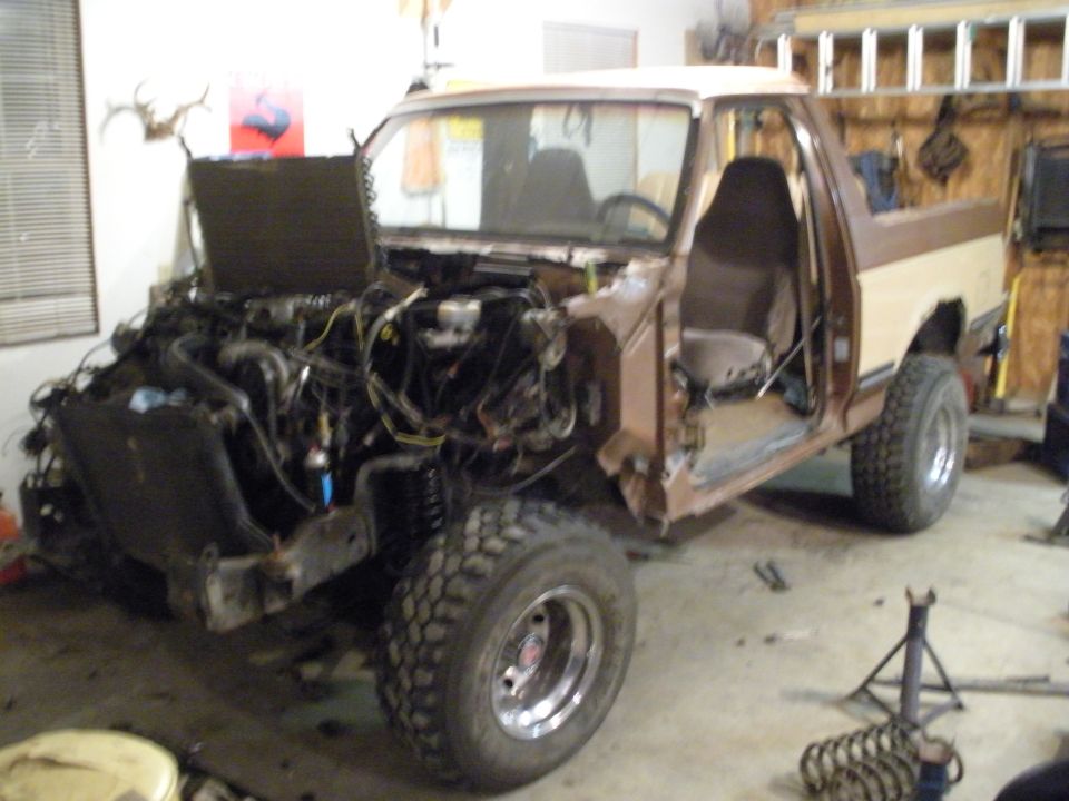 1987 Ford Bronco with hood open and engine removed, doors off, in a garage