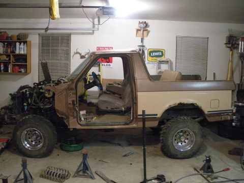 1987 Ford Bronco - A 1987 Ford Bronco is undergoing repairs in a garage, with its engine compartment disassembled.