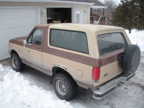 1987 Ford Bronco - This two-tone brown and tan SUV is parked in the snow with a spare tire mounted on the rear door.