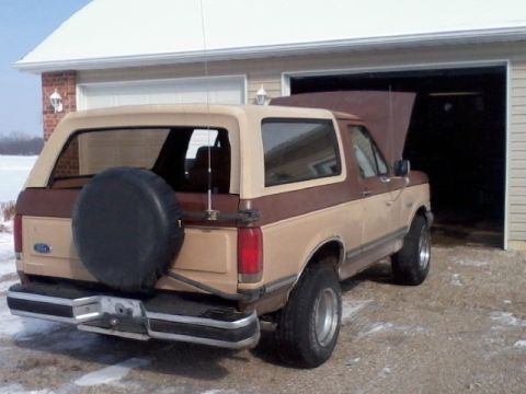 1987 Ford Bronco - Rear view of a two-tone 1987 Ford Bronco parked outside a garage in winter.