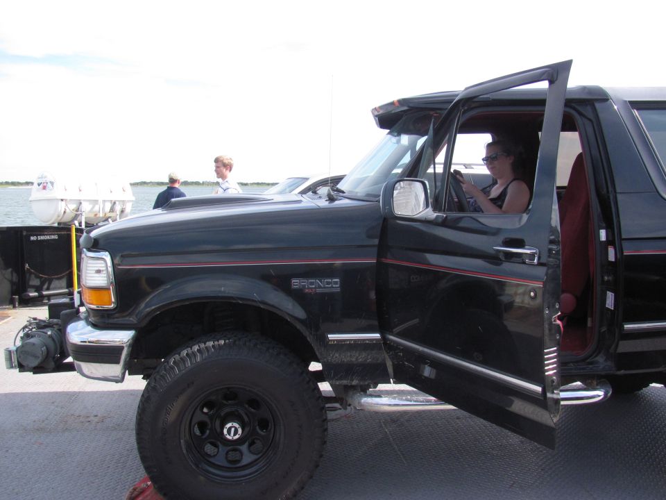 Black 1995 Ford Bronco with open doors, woman driving, on a ferry deck
