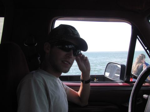 1995 Ford Bronco - A man sits in the driver's seat of a vehicle, looking out at the water.