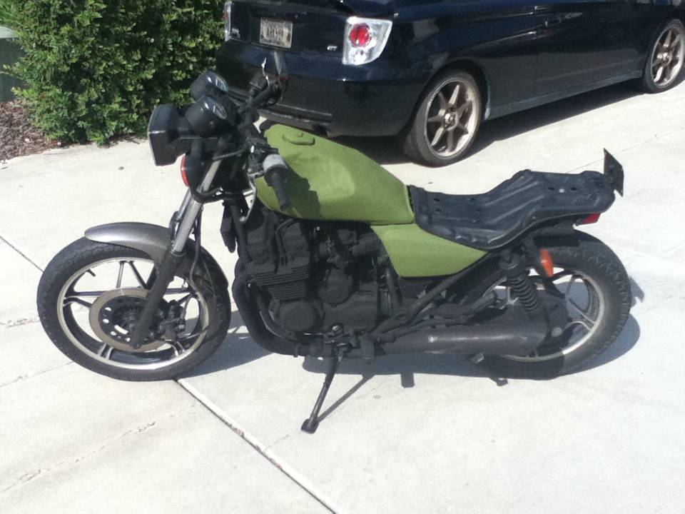 Green motorcycle with black seat and exhaust, parked next to a black car