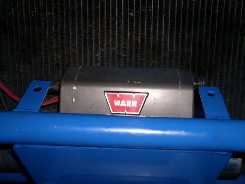 1979 Ford Bronco - Warn winch installed on a blue frame, positioned in front of a vehicle's radiator.