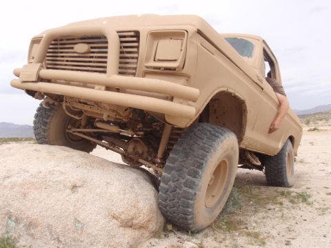 1978 Ford Bronco - This modified Ford truck is navigating challenging terrain, with its front tire on a large rock.