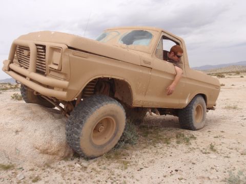 1978 Ford Bronco - A tan 1978 Ford Bronco navigates rocky terrain with a driver leaning out the window.