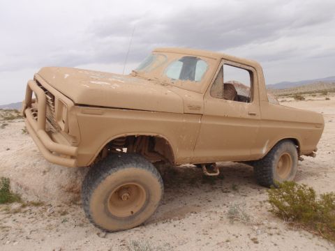 1978 Ford Bronco - A dusty 1978 Ford Bronco sits on rocky ground in a desert landscape under a cloudy sky.