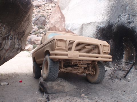 1978 Ford Bronco - This tan Ford F-Series truck is navigating a rocky off-road trail, wedged between large boulders.