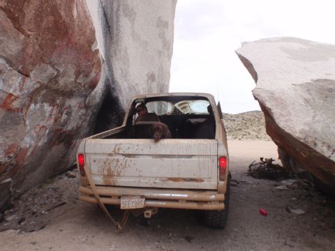 1978 Ford Bronco - A beige Ford pickup truck is wedged between two massive rocks in a desert landscape.