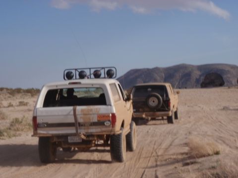 1978 Ford Bronco - Two SUVs traverse a dusty desert trail under a bright blue sky.