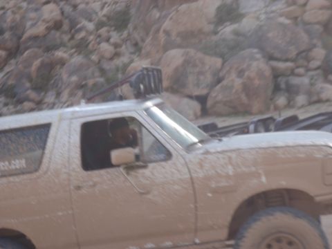 1978 Ford Bronco - A mud-splattered white Ford Bronco navigates a rocky, off-road terrain.