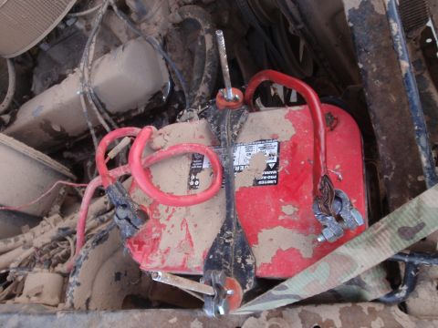 1978 Ford Bronco - Close-up of a red battery and its connected cables, covered in mud, within a vehicle's engine compartment.