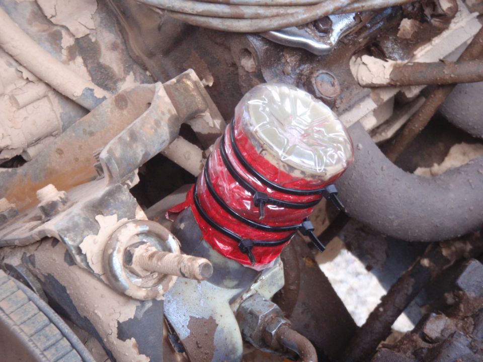 Engine component covered with red tape and plastic bottle, secured with zip ties