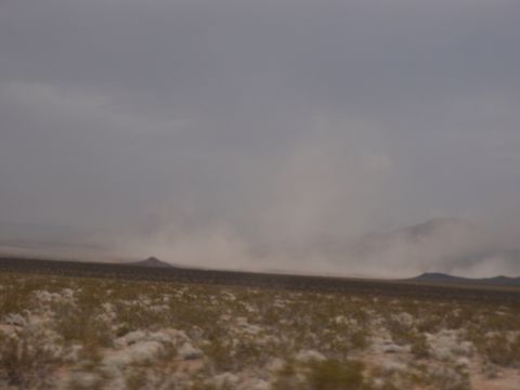 1978 Ford Bronco - A dust storm sweeps across a dry, brush-covered desert landscape under a hazy sky.