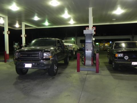 1978 Ford Bronco - Three trucks are parked at a gas station under bright lights at night.