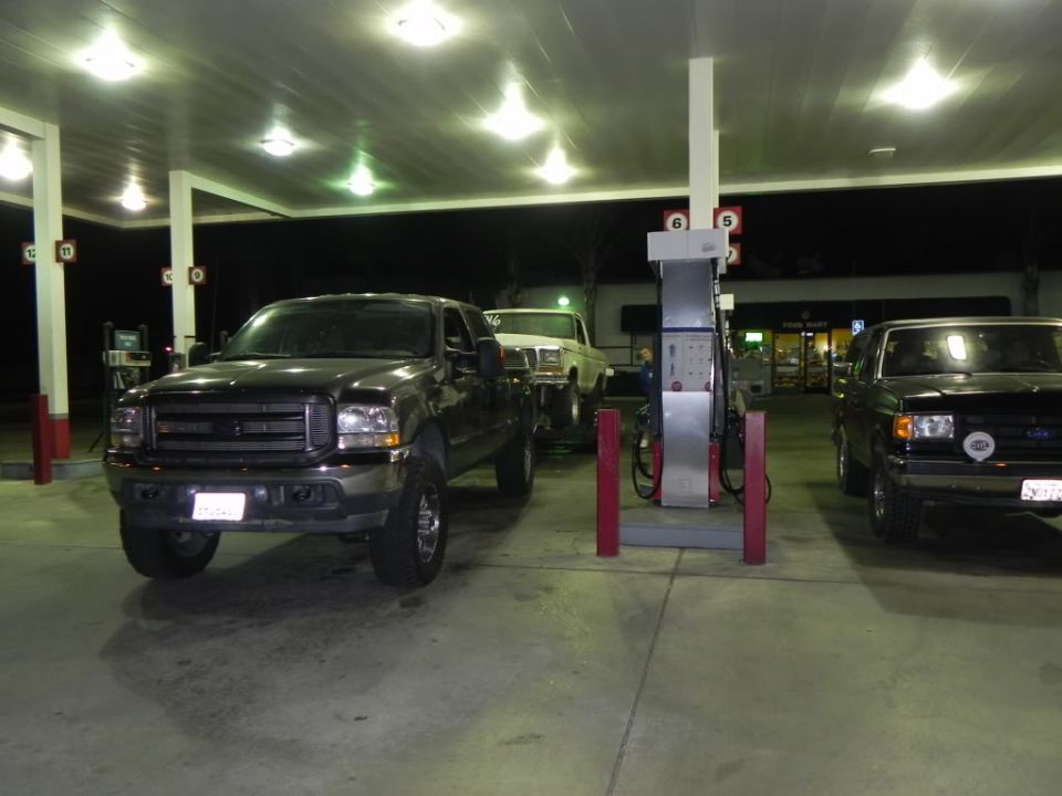 Three trucks at a gas station at night