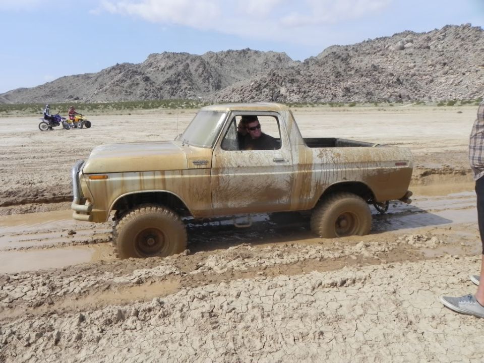 Mud-covered topless Ford Bronco stuck in a desert mud hole with driver inside