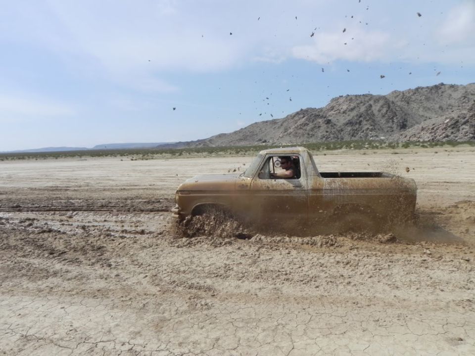Mud-covered square-body Ford pickup spraying mud across a desert dry lake bed